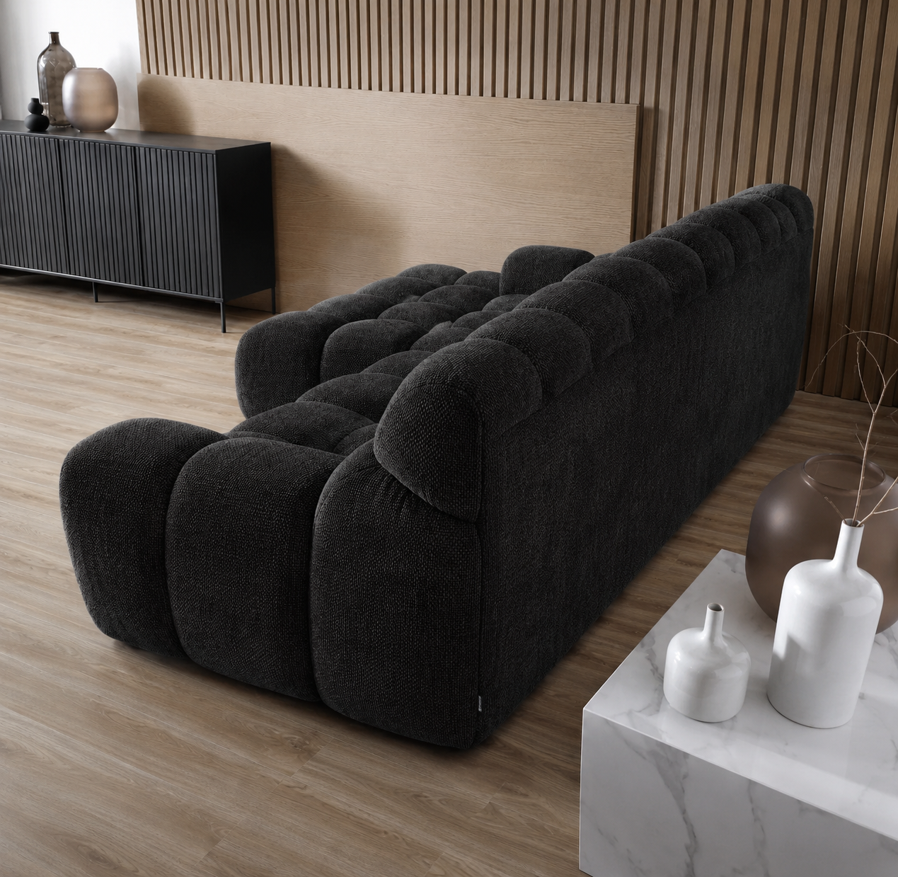 Black sofa in a modern living room with wooden floor and decorative vases.