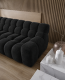 Black tufted sofa in a room with wooden walls and a marble side table.