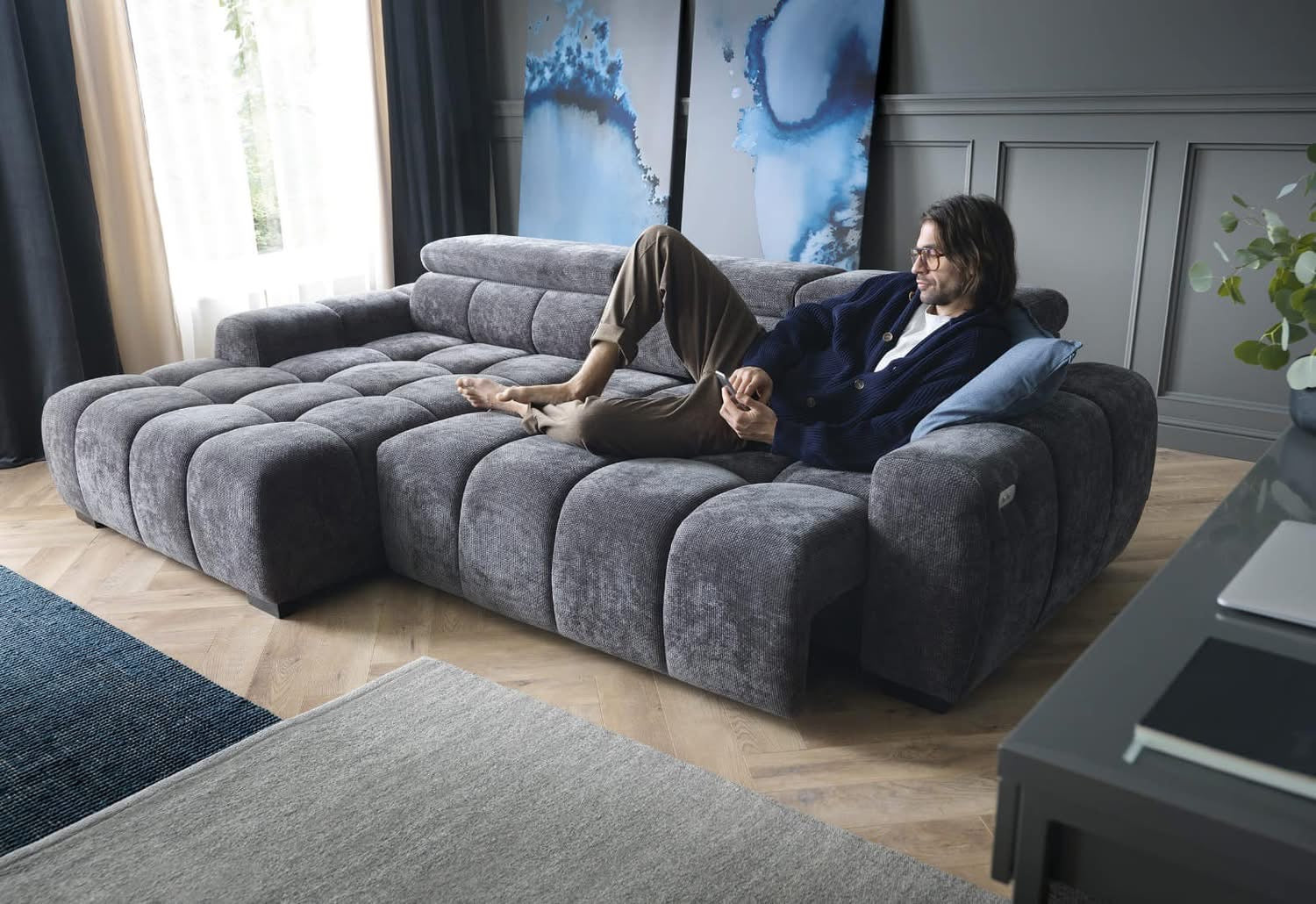 Man relaxing on a large gray BULL S corner sofa in a modern living room.