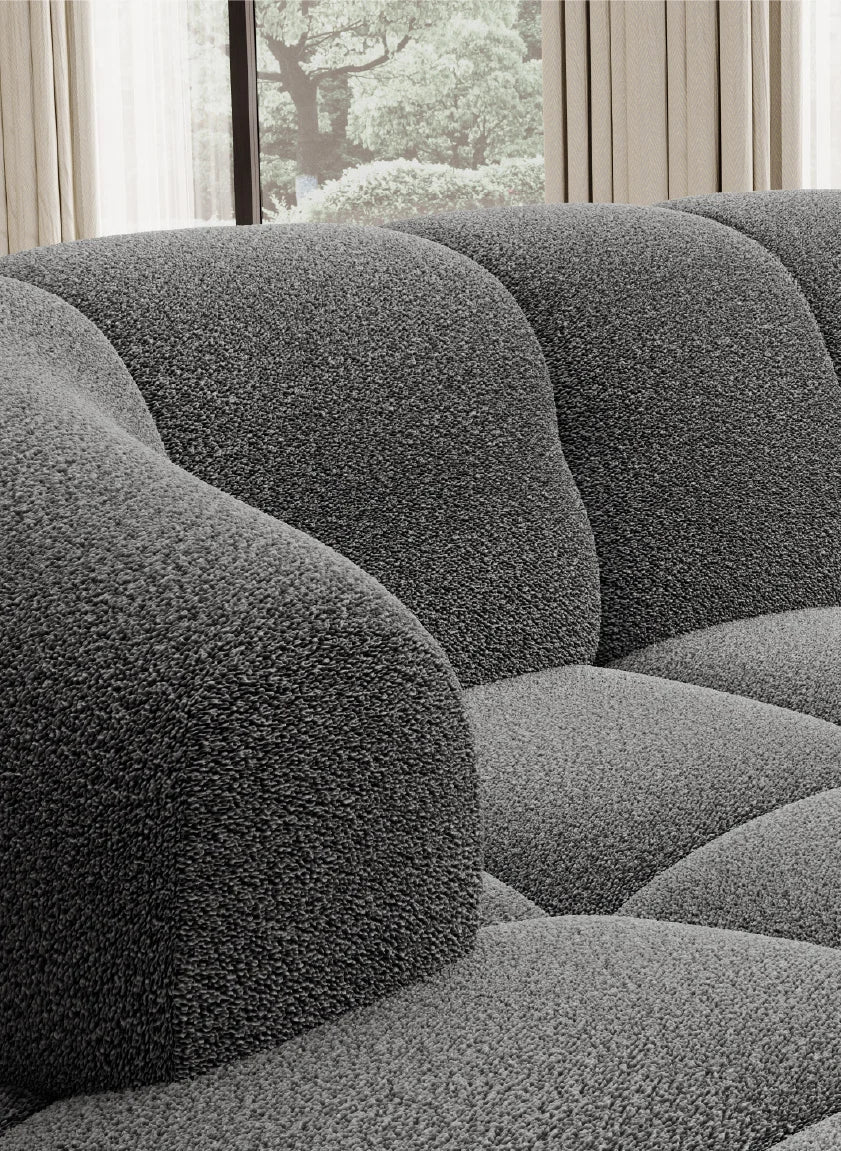 Gray textured corner sofa VELPA XL in a room with a window view of trees and light curtains.